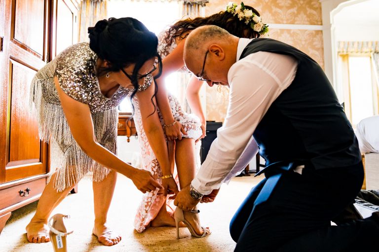 Mother of the bride and father helping the bride into her bridal shoes